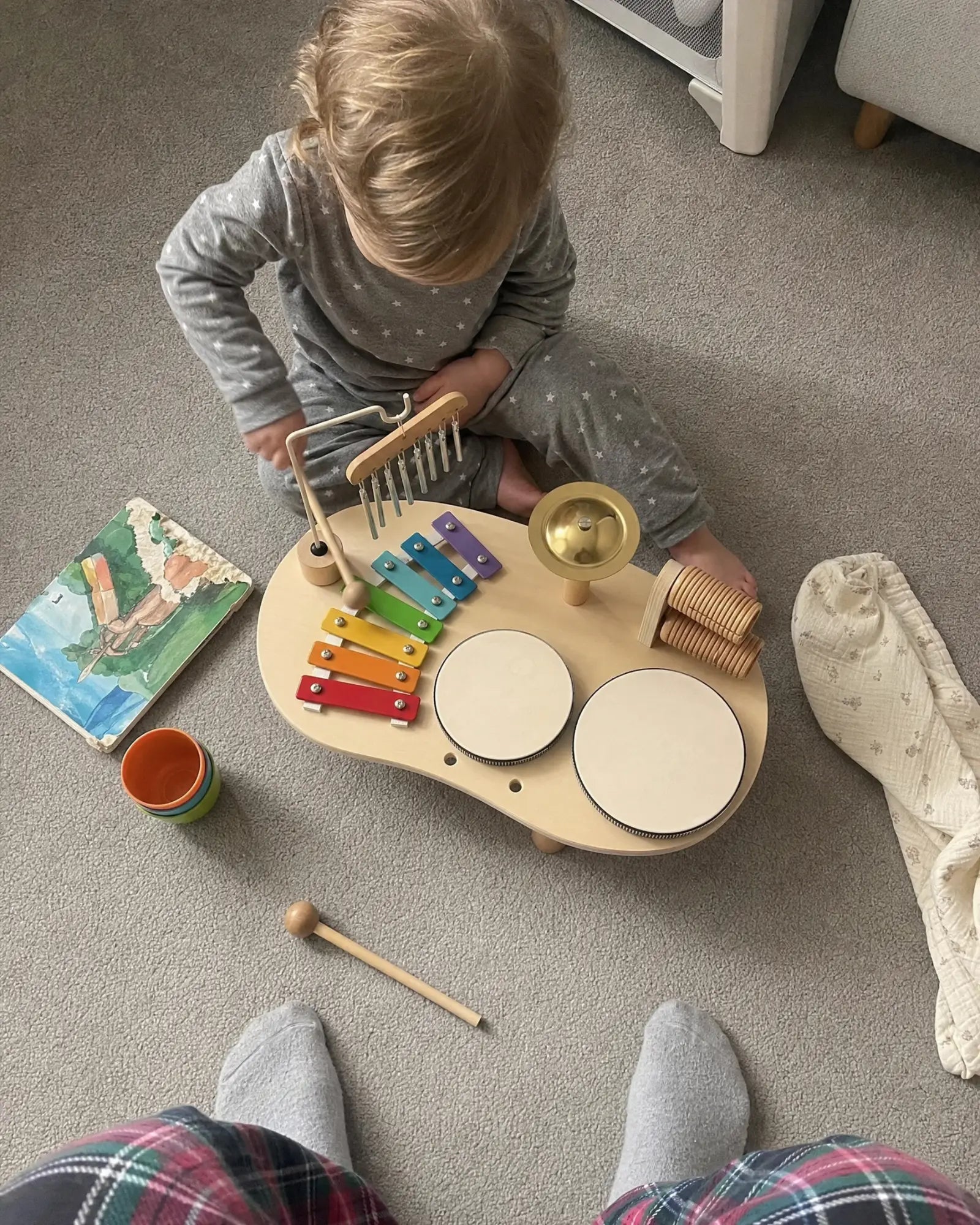 Top-down view of a toddler at the music table showing the drums, xylophone, chimes, cymbal and scraper